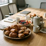 A meeting-room table set with a platter of pastries, fruit and coffee