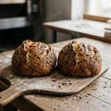 Two seeded sourdough loaves on a wooden peel, fresh from the oven