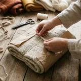 Hands wrapping a folded oat wool throw in brown paper and tying it with twine
