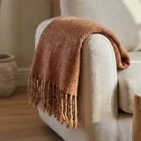 A rust herringbone wool throw draped over the arm of a pale linen sofa
